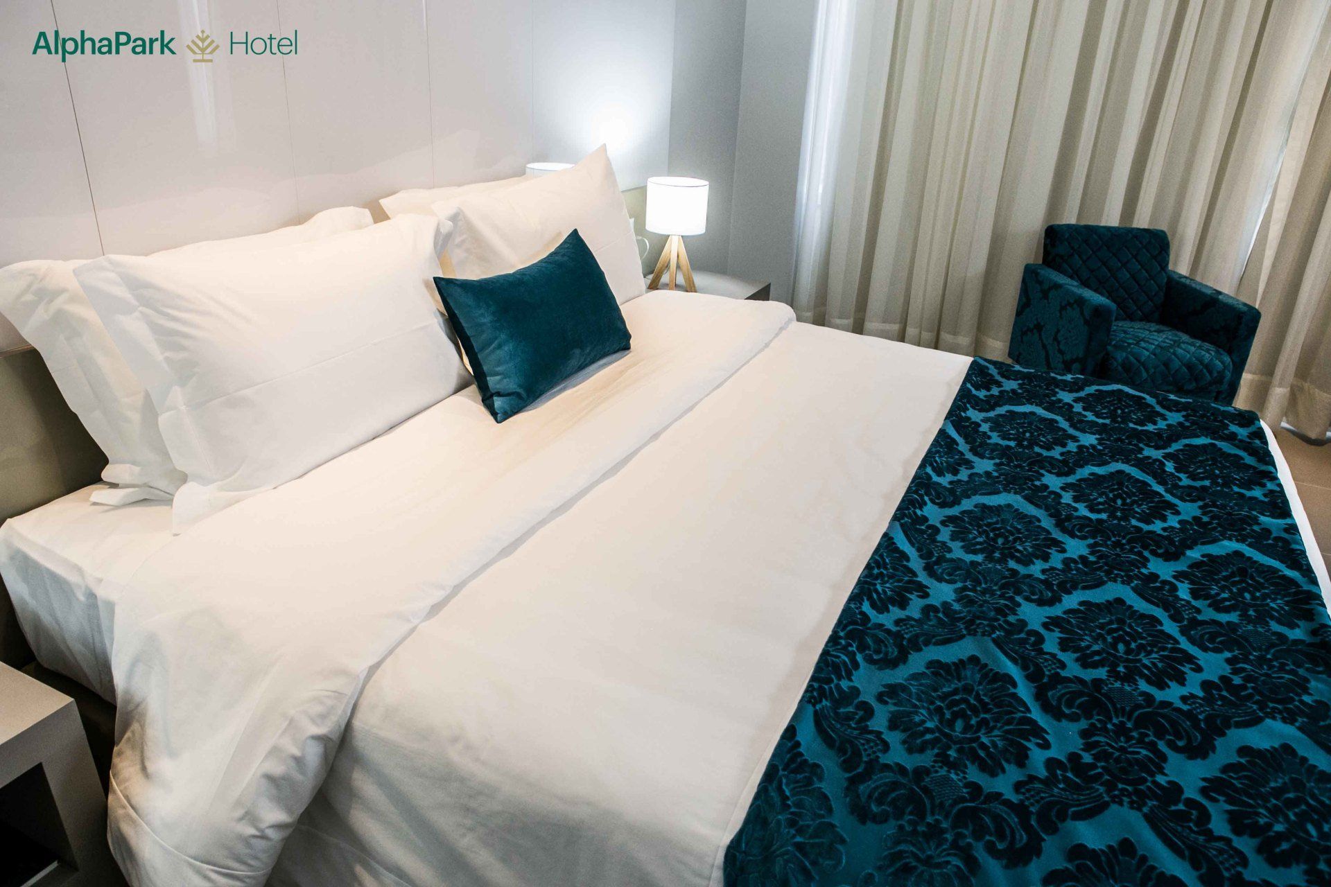 Um quarto de hotel com uma cama, cadeira e luminária.