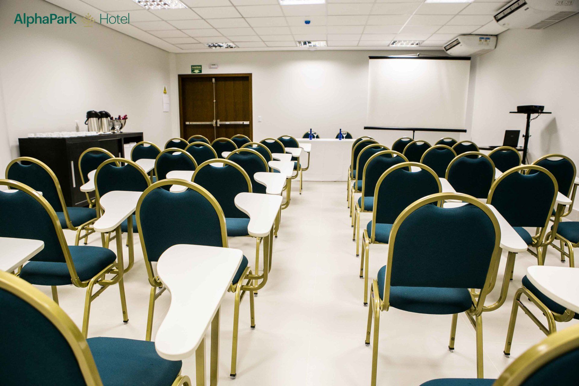 Fileiras de cadeiras e mesas em uma sala de aula com a palavra alphapark na parede
