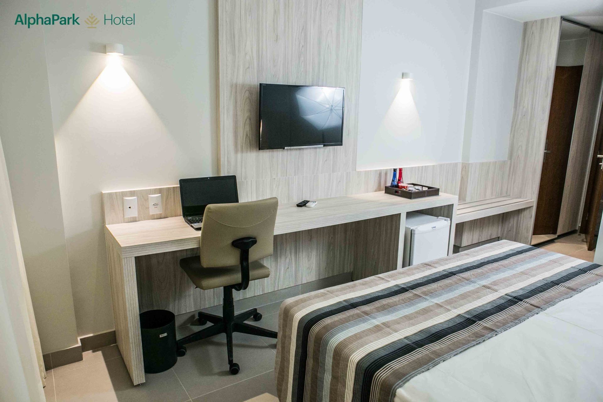 Um quarto de hotel com uma cama, escrivaninha, cadeira e televisão.