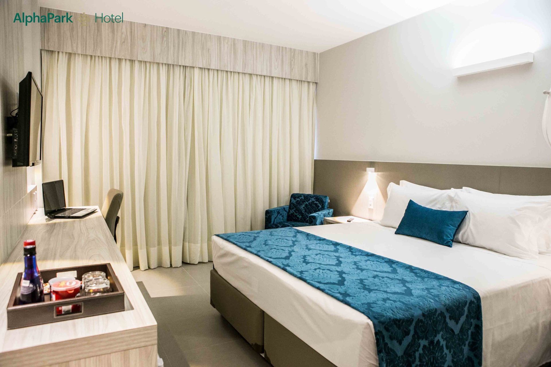 Um quarto de hotel com uma cama king size, escrivaninha, cadeira e televisão.
