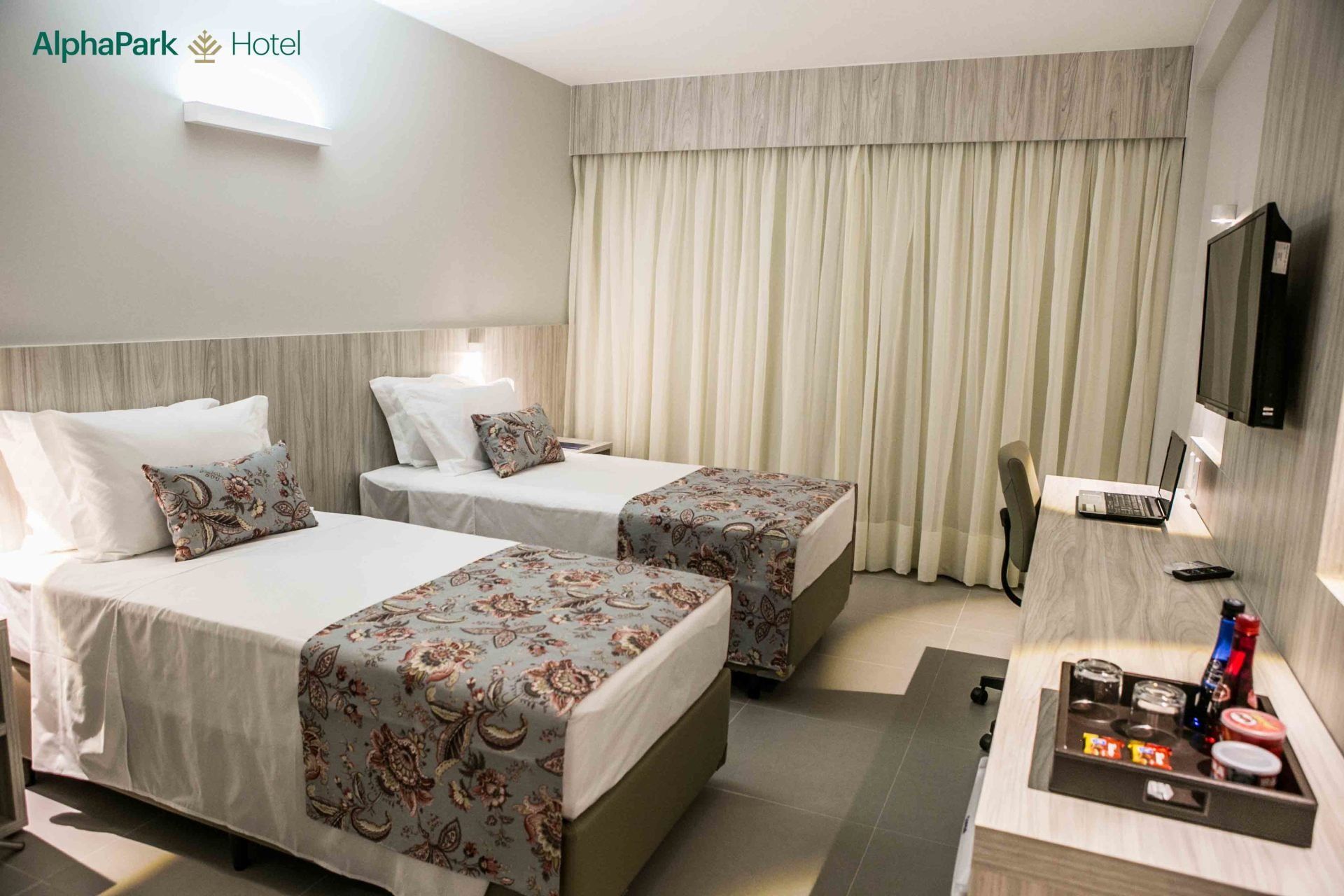 Um quarto de hotel com duas camas, uma escrivaninha e uma televisão.