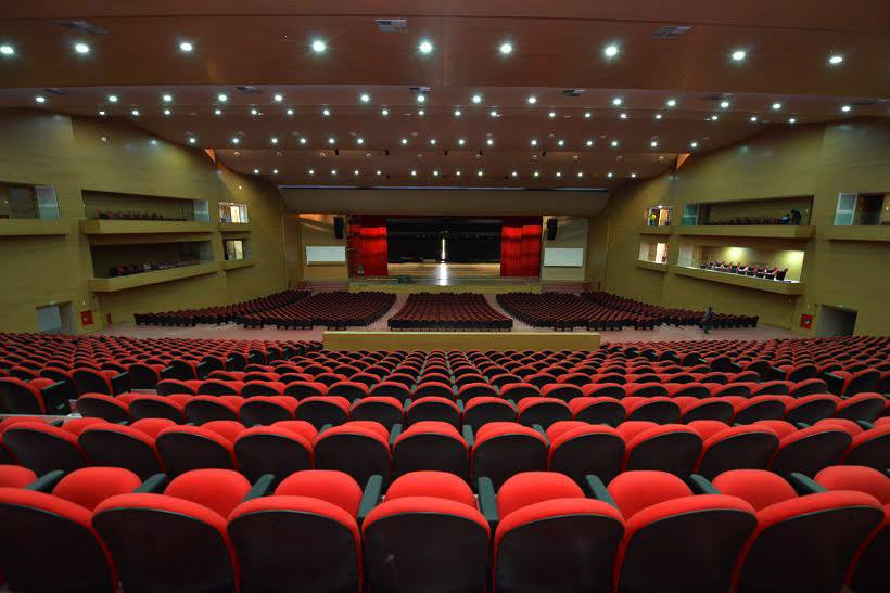 Um grande auditório cheio de fileiras de assentos vermelhos e um palco.