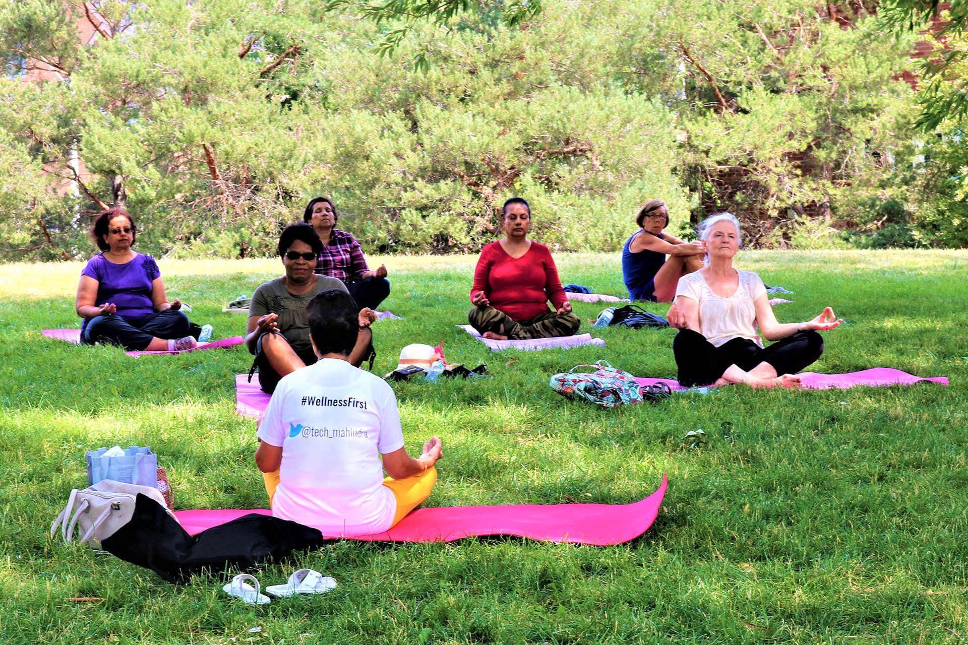 A group of people are sitting on yoga mats in a park.