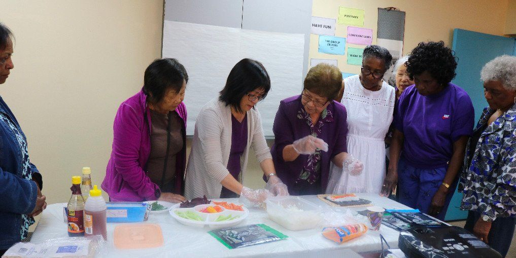 A group of women are standing around a table preparing food.