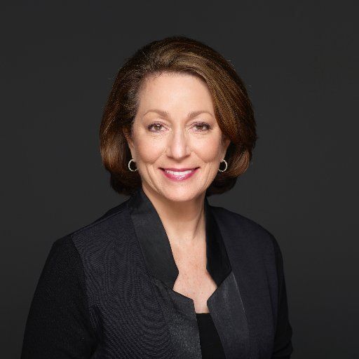 A woman in a black jacket and earrings is smiling for the camera.