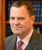 A man in a suit and tie is standing in front of a bookshelf.