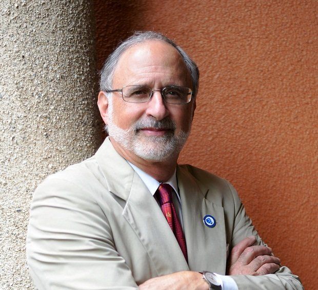 A man with glasses and a beard is standing with his arms crossed