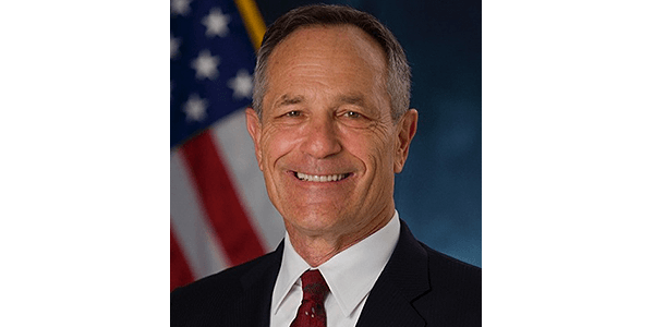 A man in a suit and tie is smiling in front of an american flag.