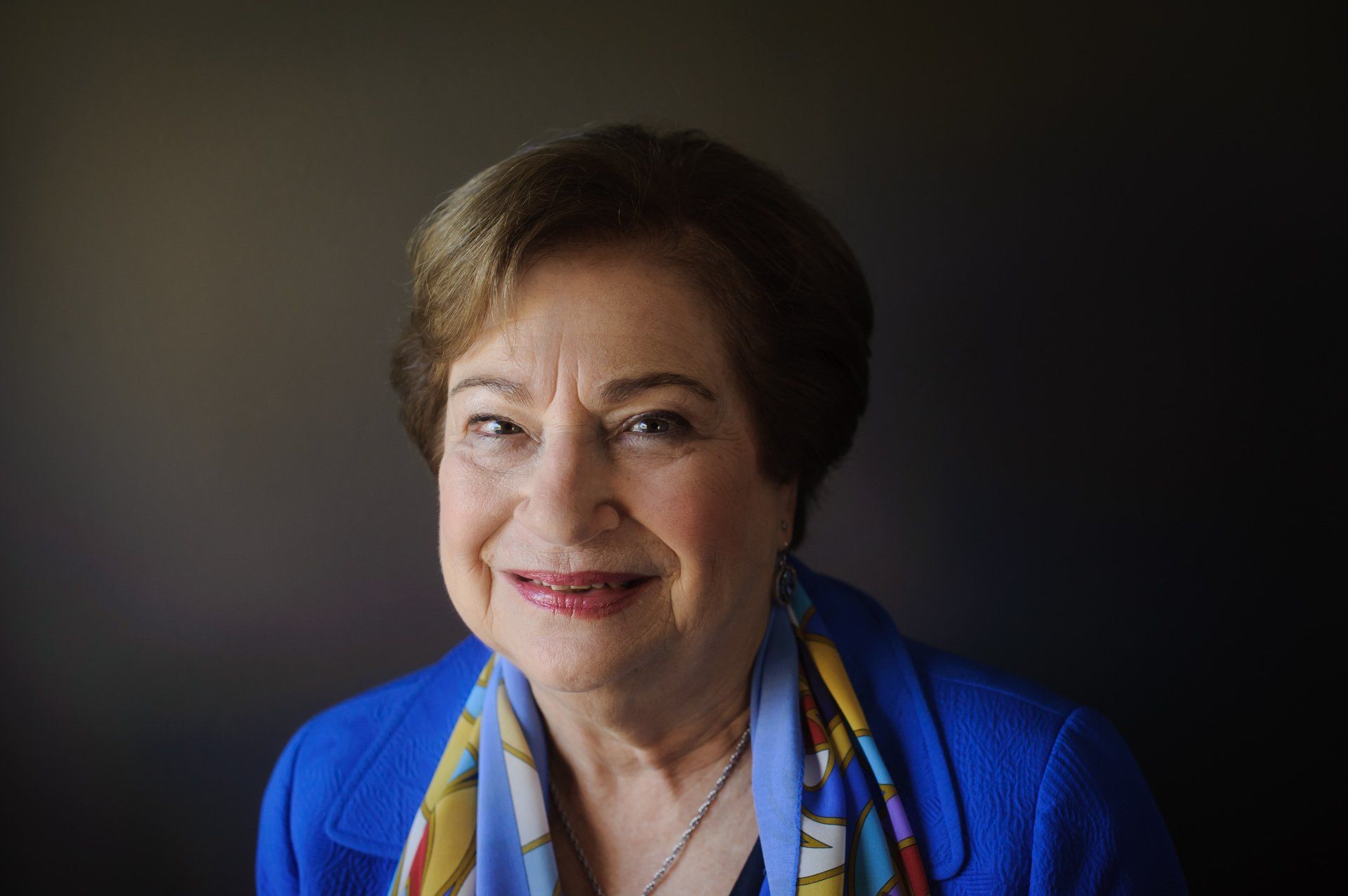 A woman in a blue jacket and scarf is smiling for the camera.