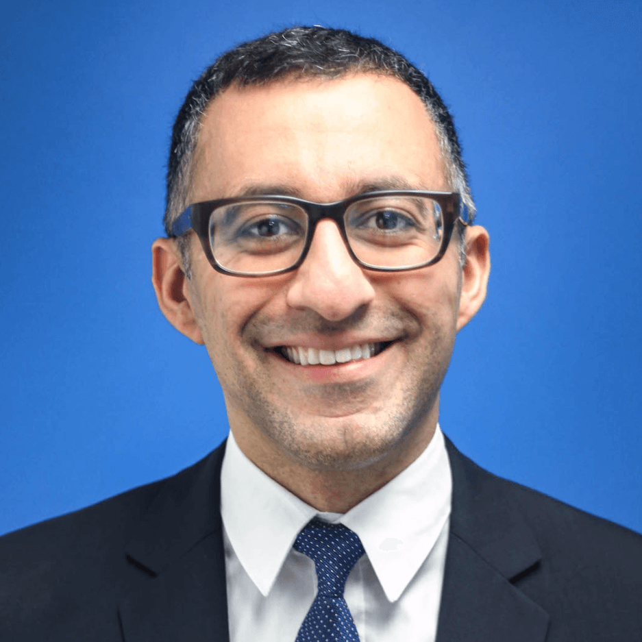 A man wearing glasses and a suit and tie is smiling for the camera.