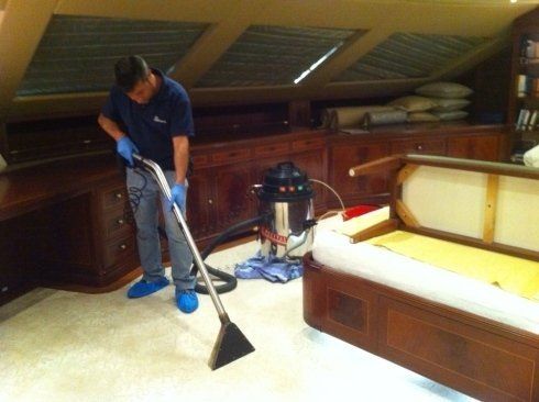 Una persona passa l'aspirapolvere in una stanza con la moquette, accanto a una struttura di letto in legno.