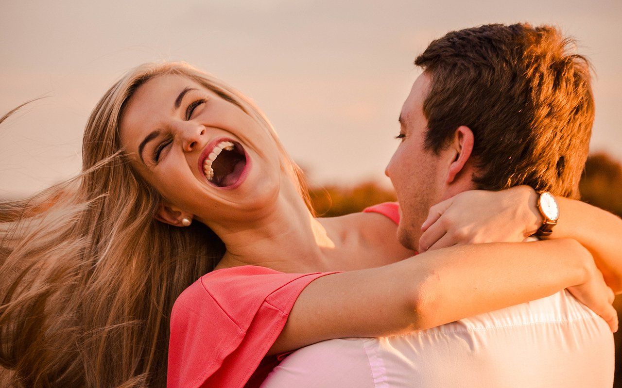 A man is carrying a woman on his shoulders and they are laughing.