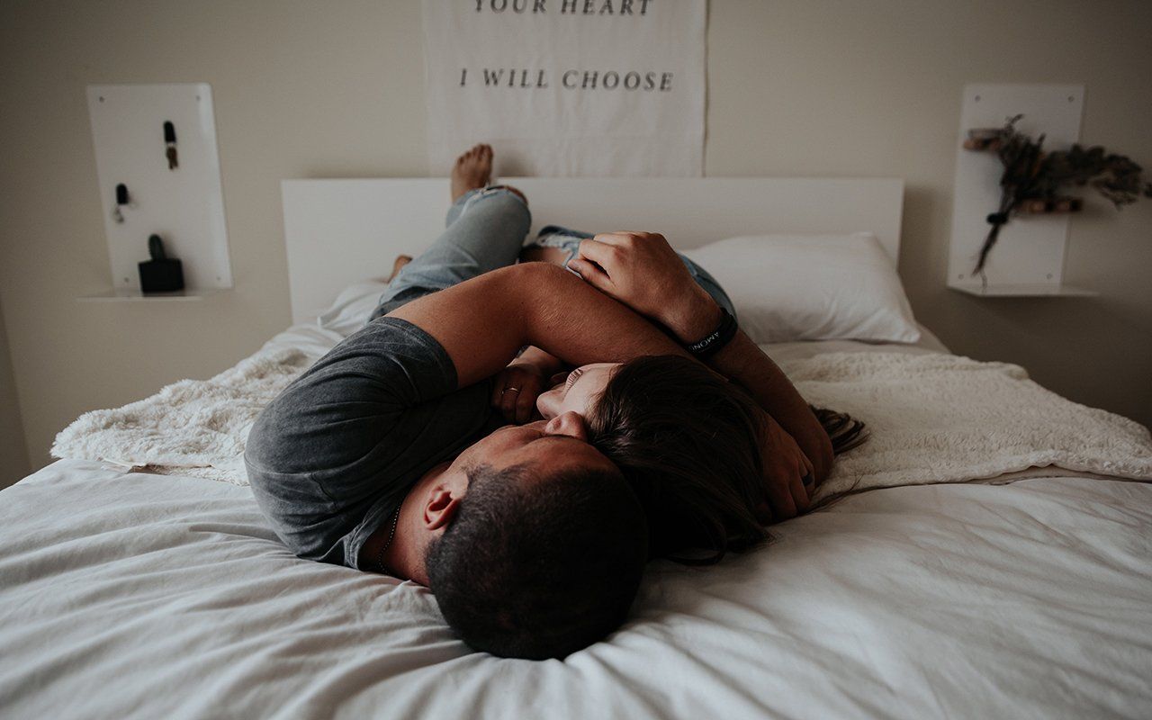 A man and a woman are laying on a bed hugging each other.