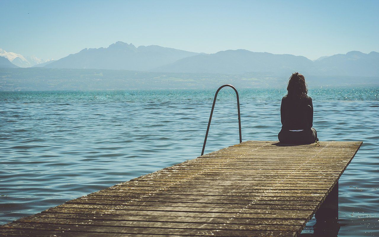 A woman is sitting on a dock overlooking a lake.