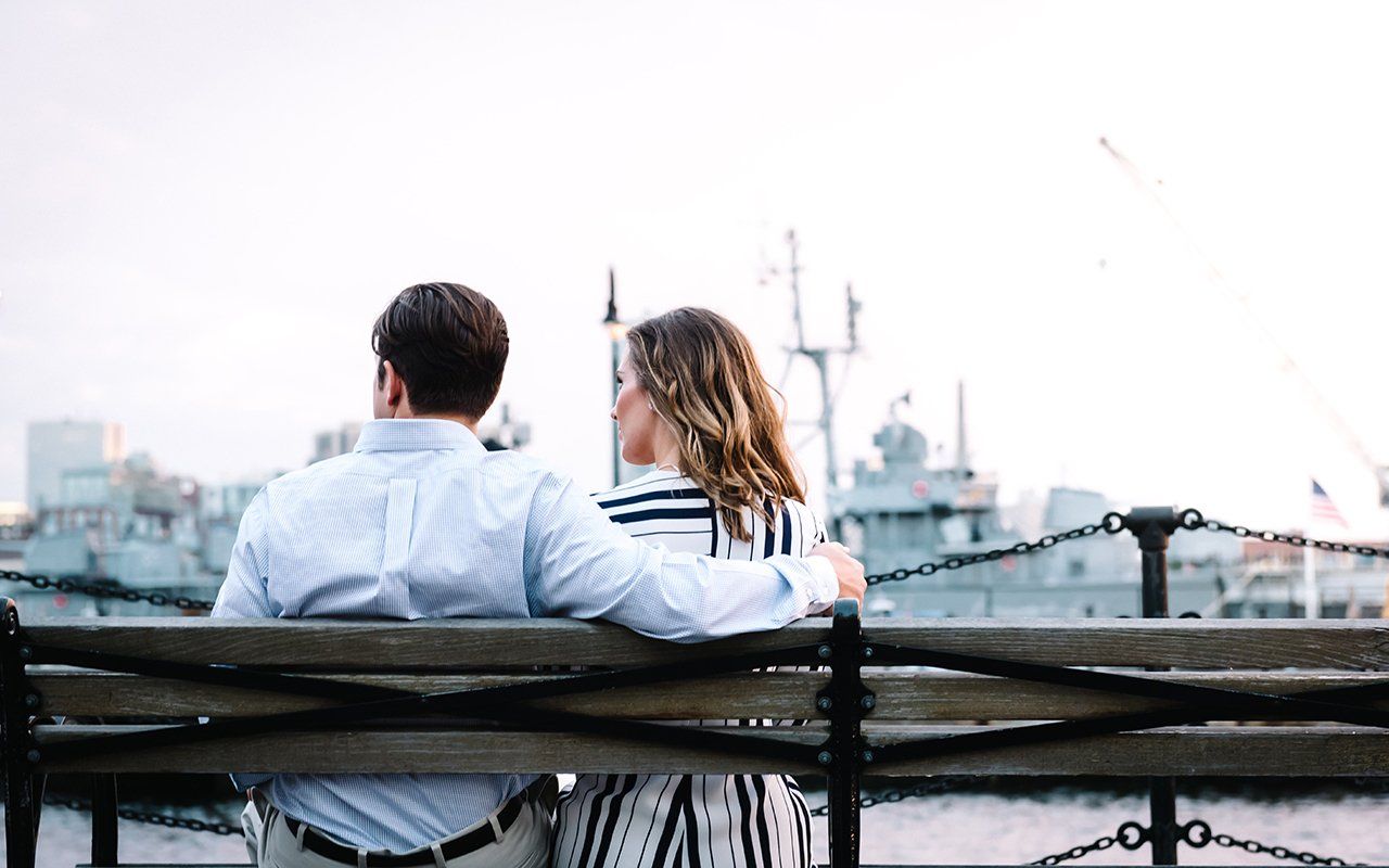 A man and a woman are sitting on a bench overlooking a body of water.