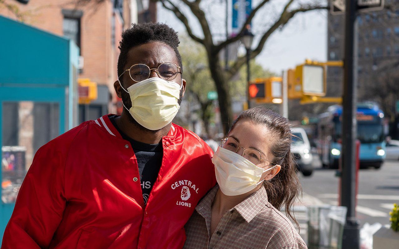 A man and a woman wearing face masks are standing next to each other on a sidewalk.