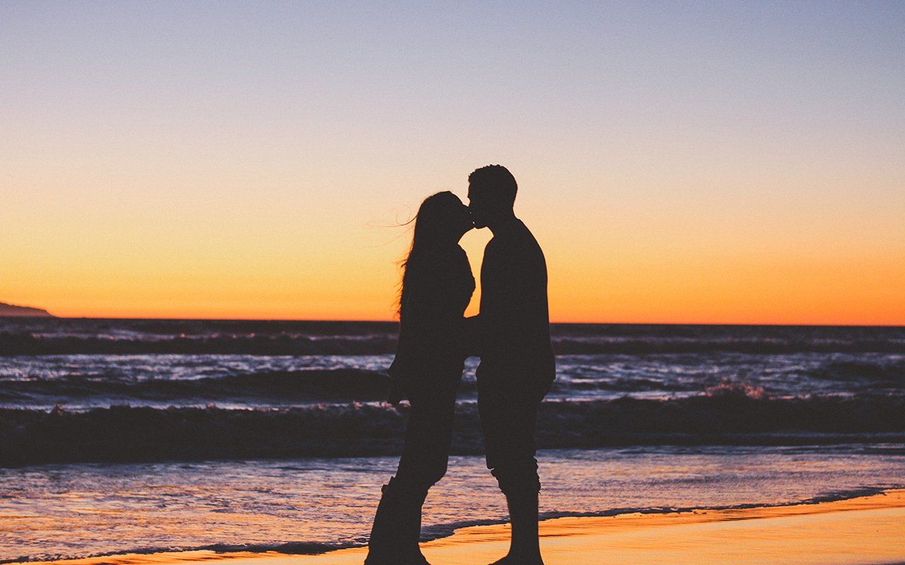 A man and a woman are kissing on the beach at sunset.
