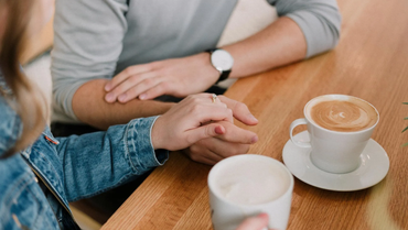 A man and a woman are holding hands while sitting at a table with a cup of coffee.
