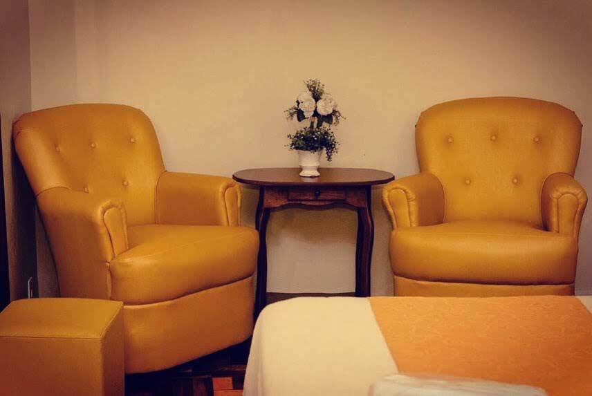 Duas poltronas amarelas com uma pequena mesa redonda e flores em um quarto aconchegante.
