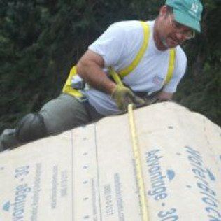 A man is measuring a large piece of cardboard with a tape measure.