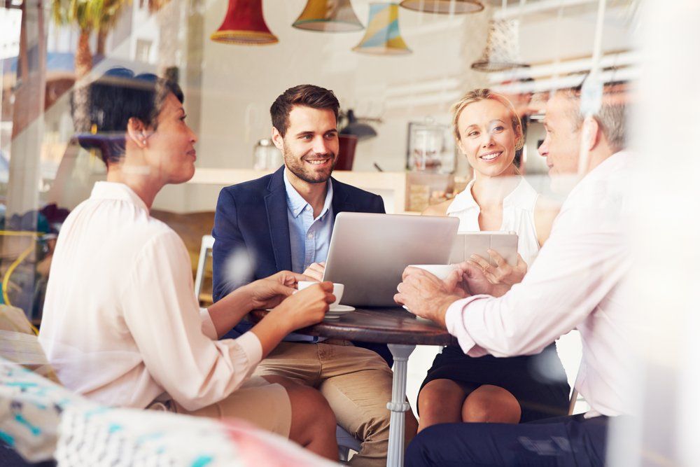 A group of people are sitting around a table with a laptop.