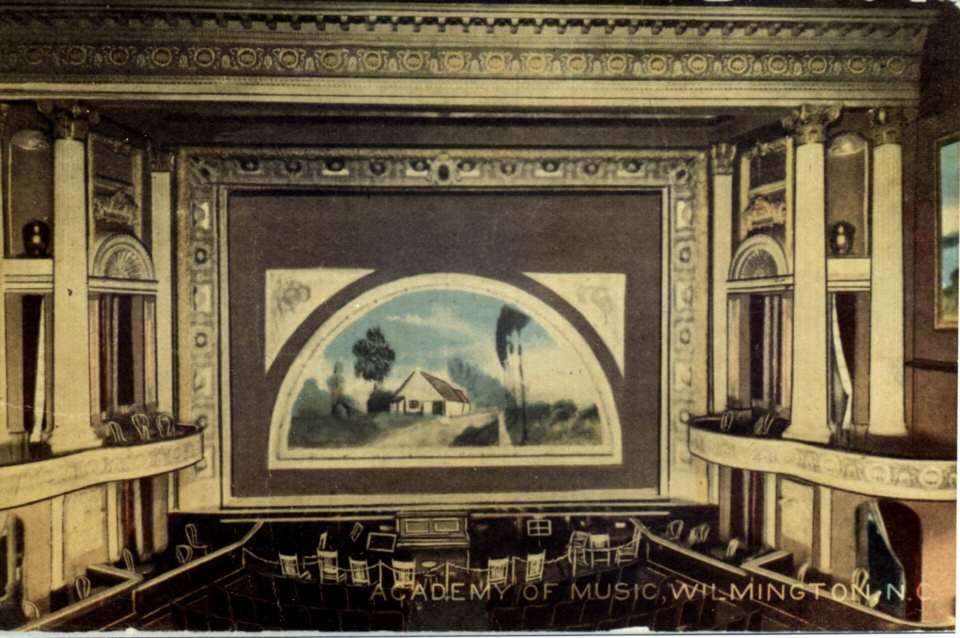 Vintage theater interior with ornate balconies and a painted stage backdrop of a seaside village.