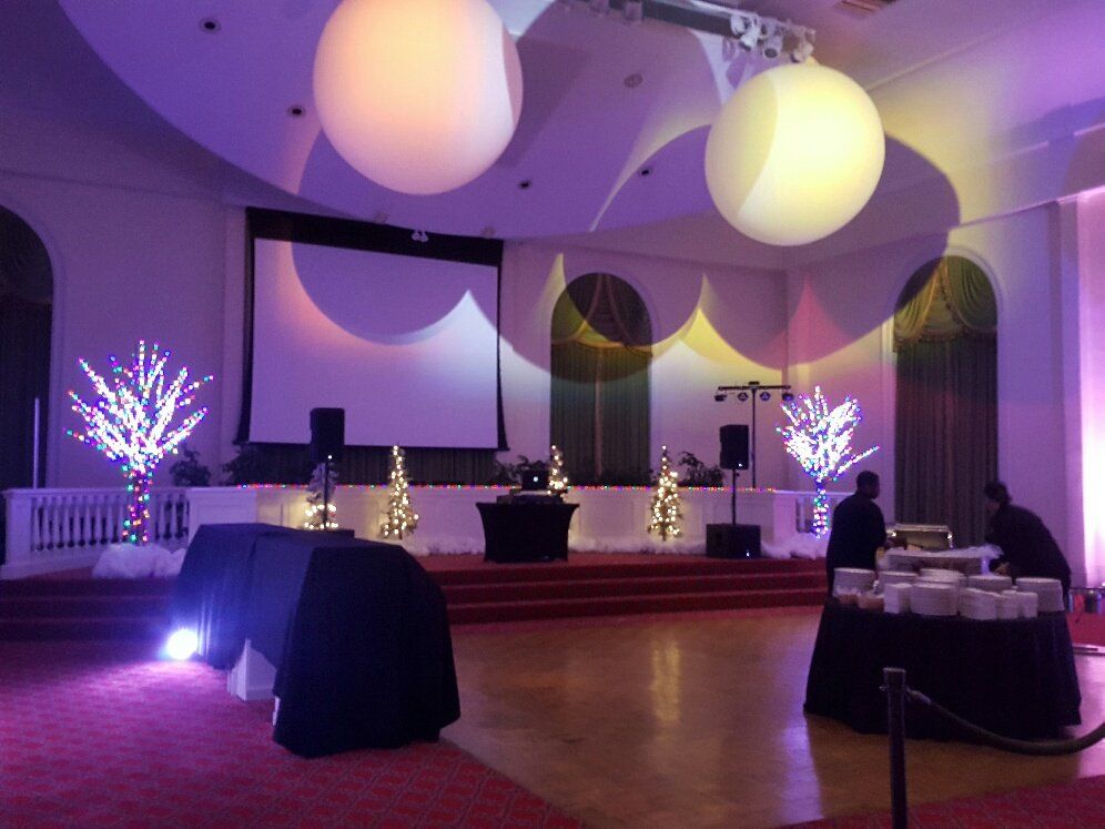 Purple-lit event hall with a stage, projection screens, hanging globe lights, and decorated tables