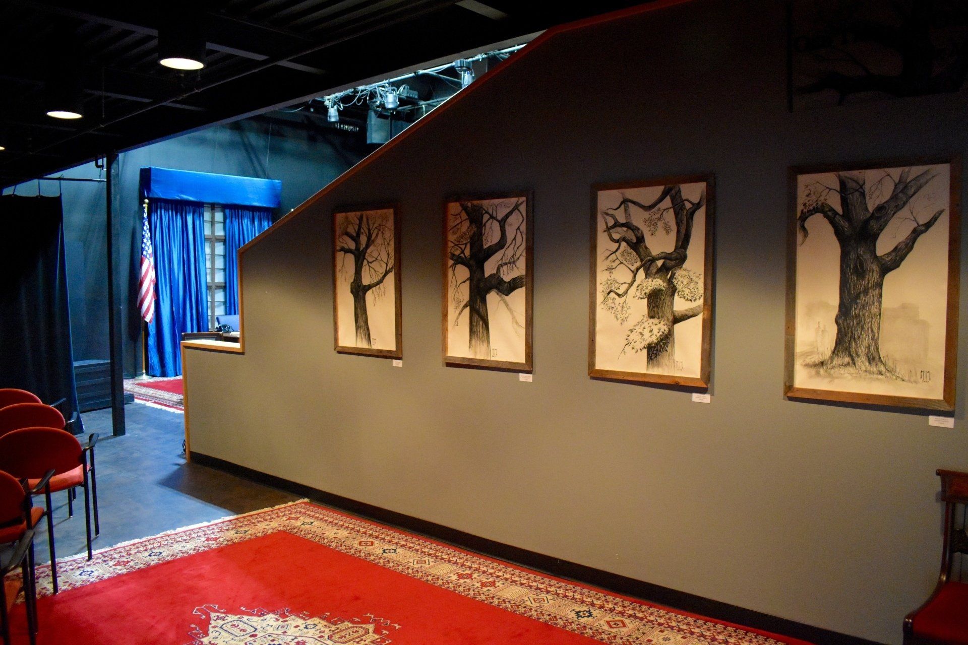 Art gallery hallway with framed tree drawings on a beige wall and a red carpet runner.