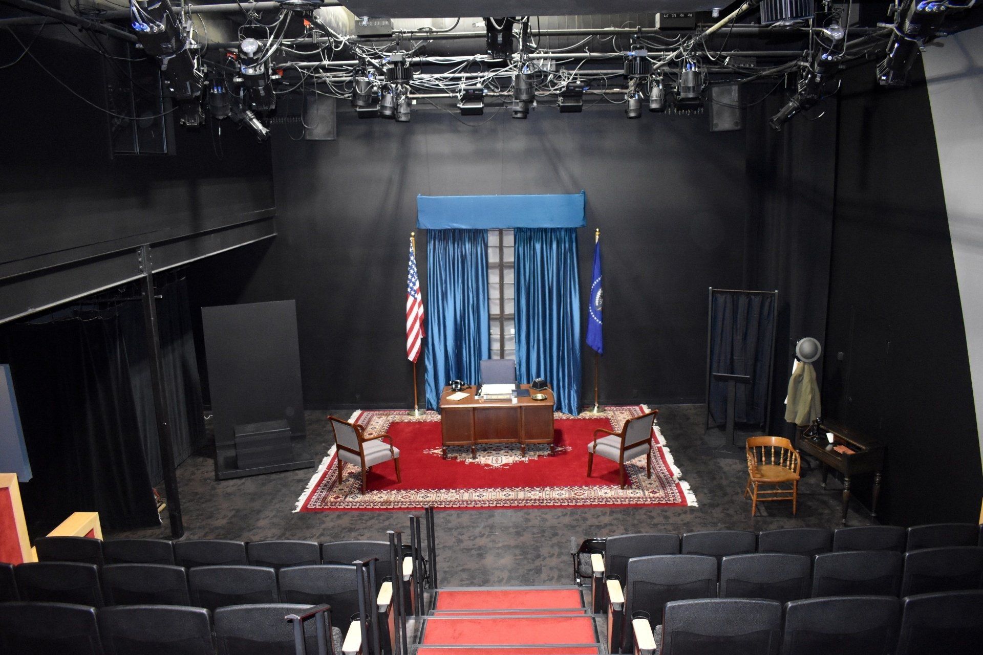 Empty theater stage with podium, blue curtains, American flag, and red carpeted aisle