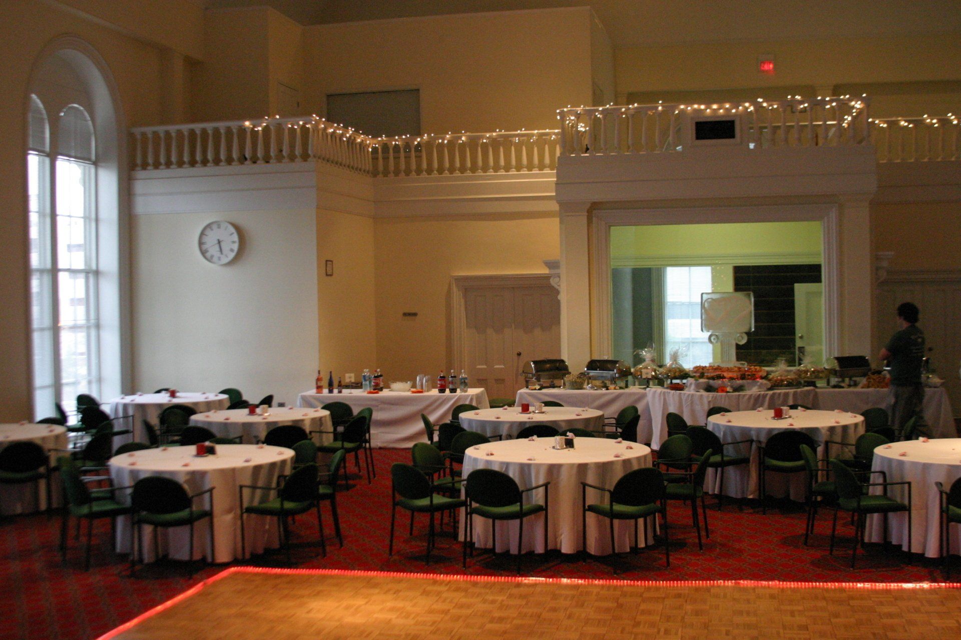 Banquet hall with round tables, white tablecloths, and string lights along a raised stage area