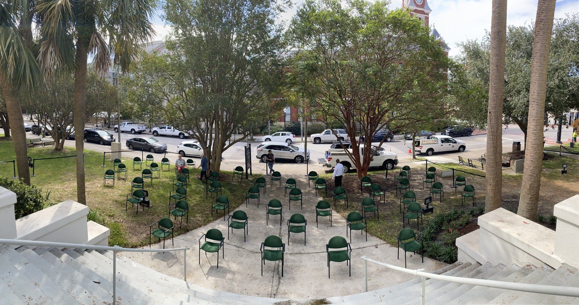Outdoor amphitheater with green chairs facing a tree-lined park and parked cars beyond