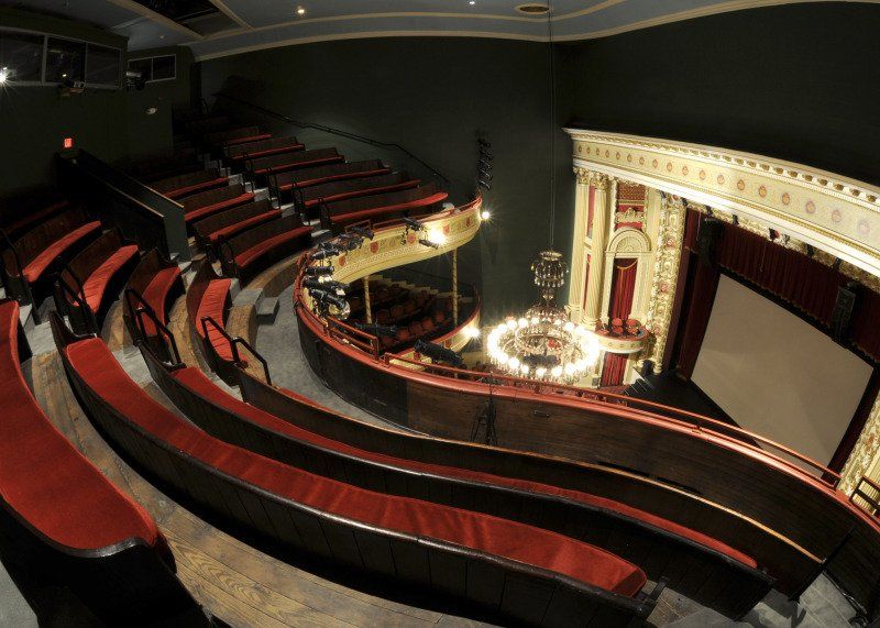 Empty theater with curved red seats and ornate gold stage balcony