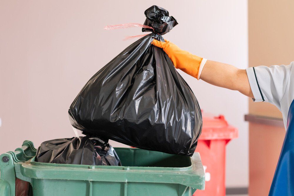 A cleaner holing a rubbish bag and throwing it into a waste collection bin