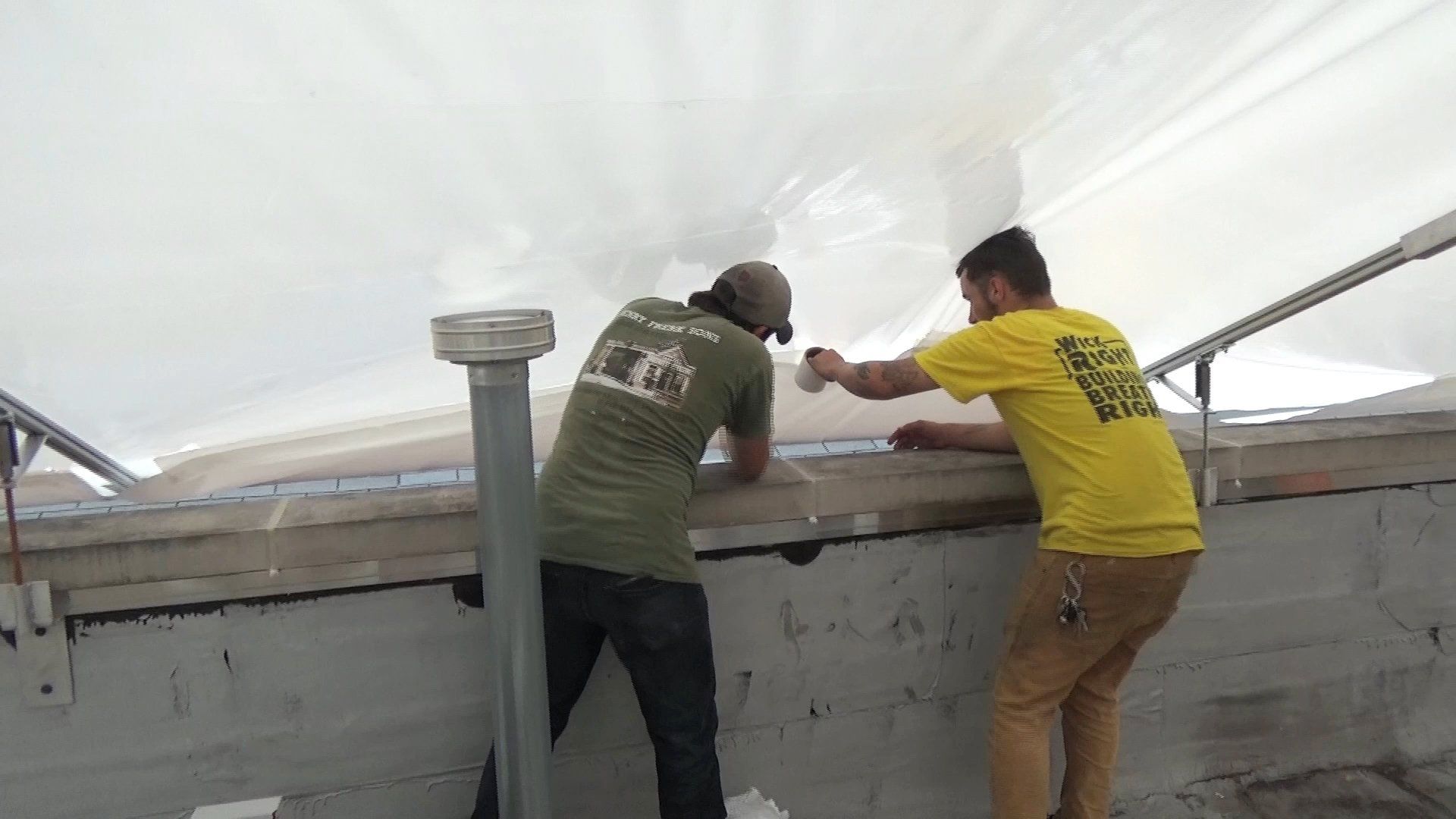 Two workers adjusting construction grade 12mm shrinkwrap of construction tent