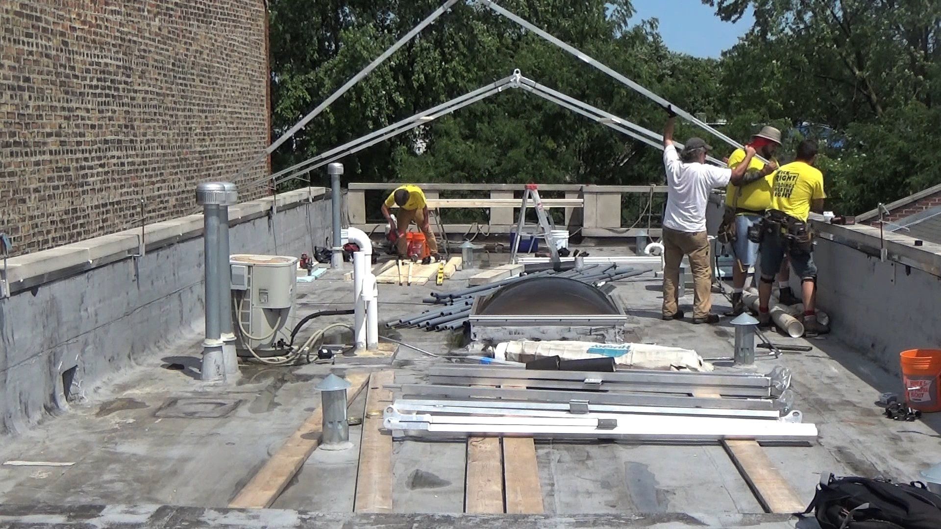 Workers on a rooftop construction site installing metal framing for construction tent