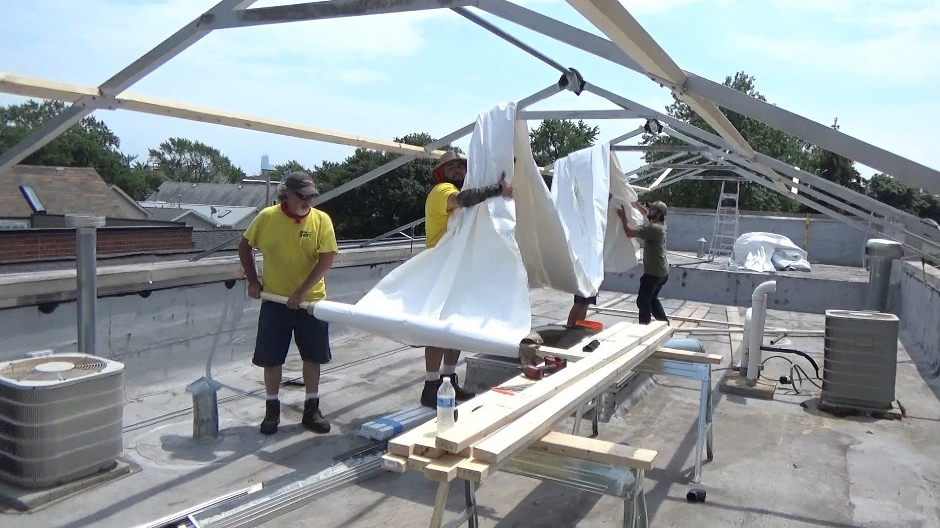 Workers hoisting construction grade 12mm shrinkwrap on metal frame beams for construction tent
