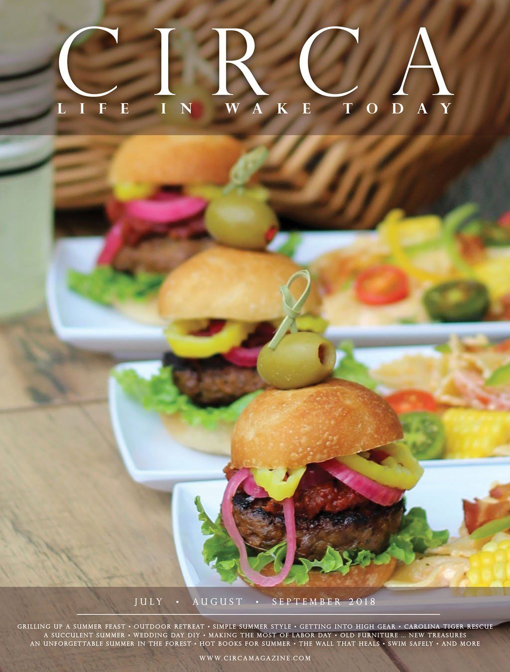 Mini burgers with olives, colorful toppings, and lemonade on a table, Circa magazine cover.