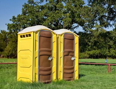 Two Yellow Portable Toilets at a Park — Kenedy, TX — Amron Pumping Services Two Yellow Portable Toilets at a Park — Kenedy, TX — Amron Pumping Services