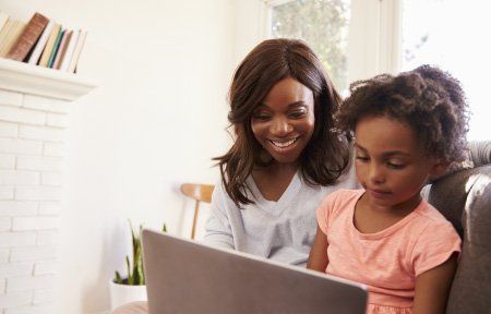 Woman smiles with child as they look at a laptop screen together in a living room.