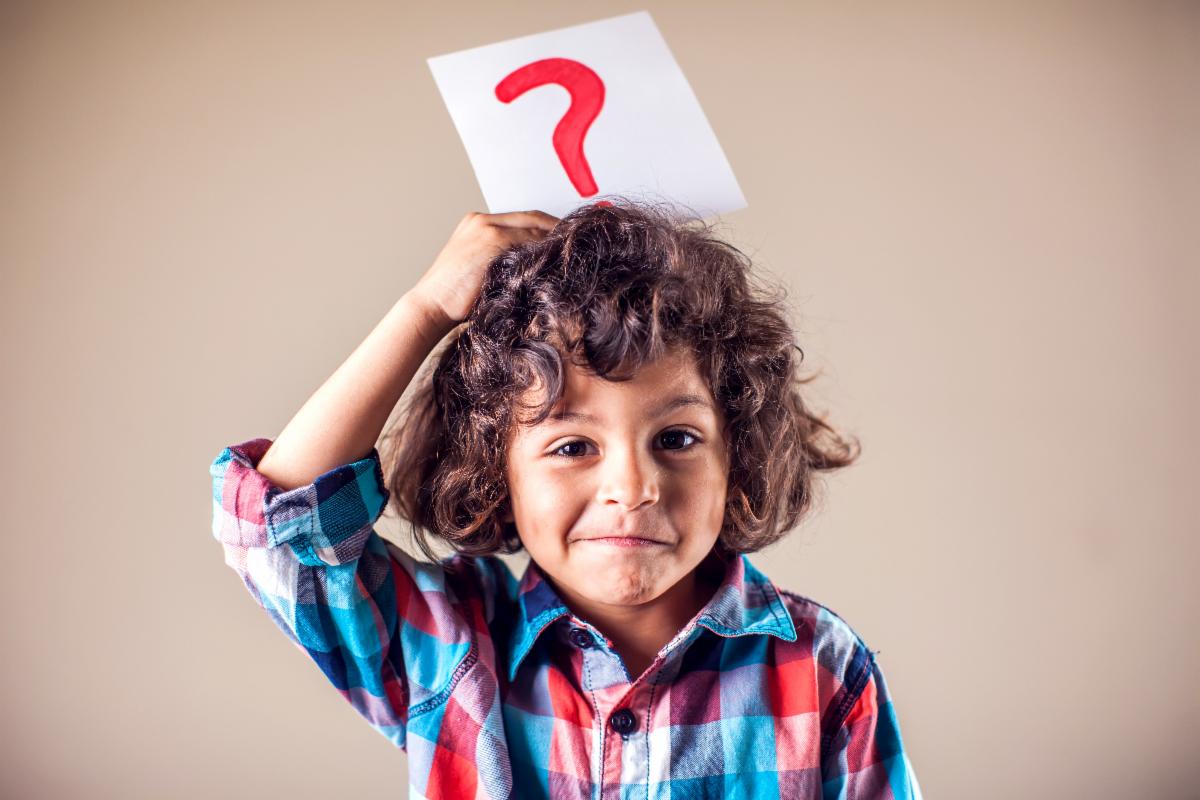 Boy with curly brown hair holding a question mark above his head, looking puzzled.