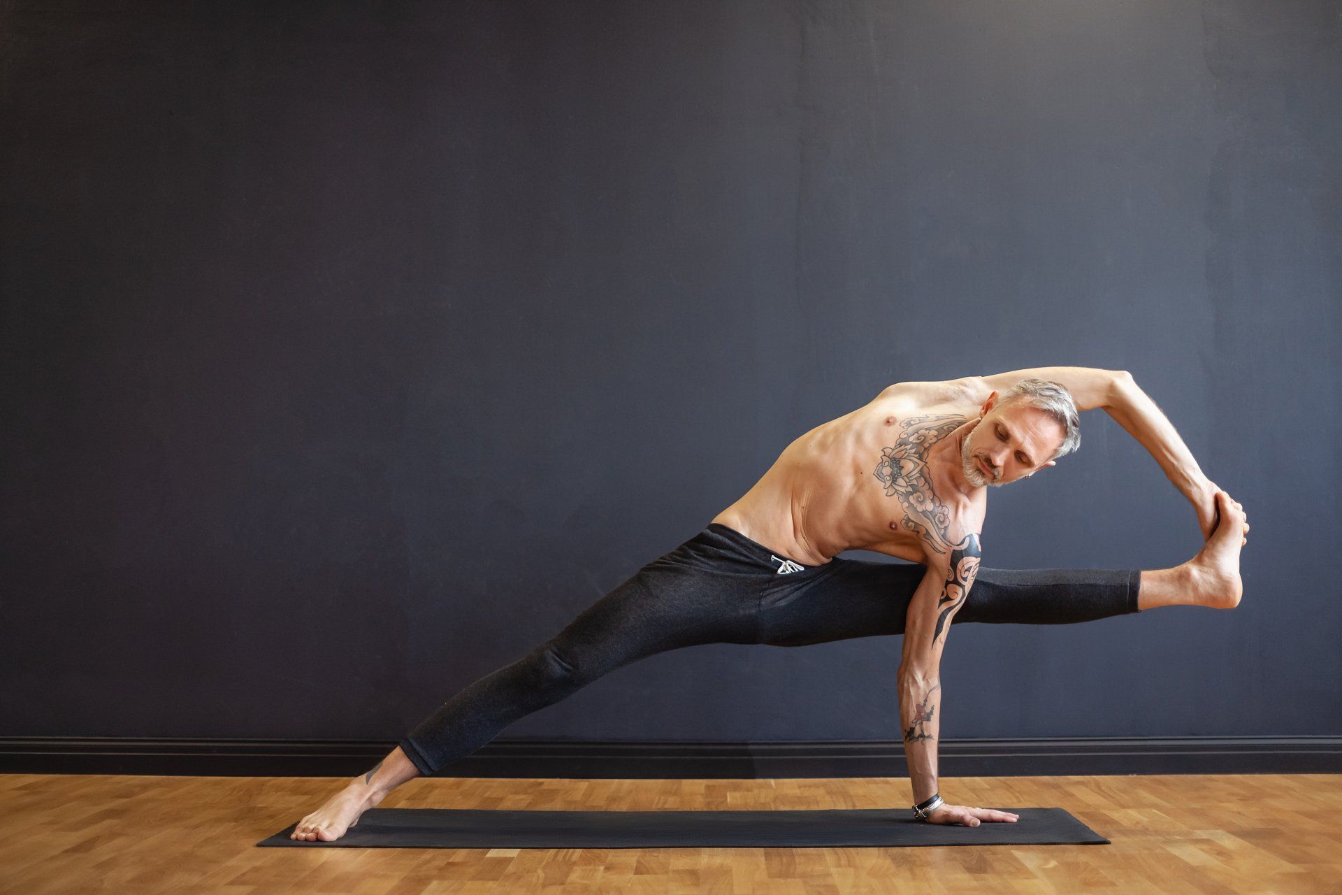 Man in a yoga pose, bending sideways, touching his foot, and looking at the camera.