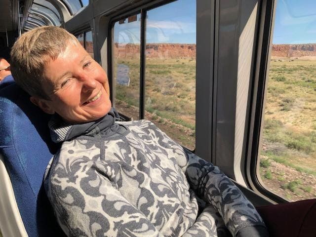 Woman smiles, looking out train window at desert landscape.
