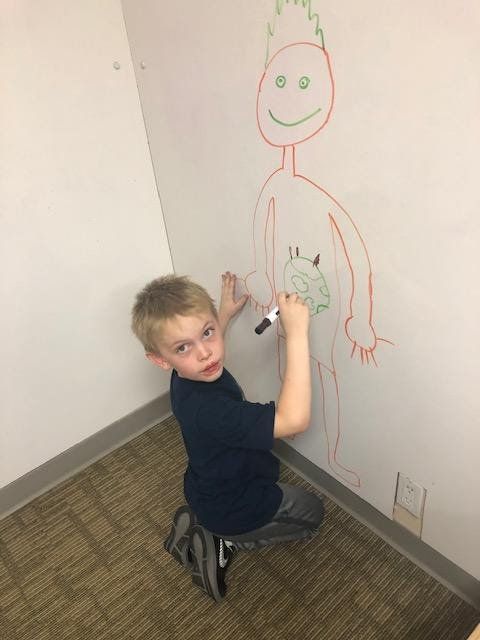 Boy drawing on a white wall with a green and red marker, making a figure.