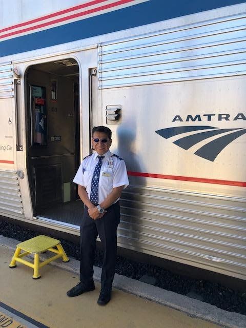 Amtrak employee standing near train car entrance. Blue, silver, and red train; yellow step stool.