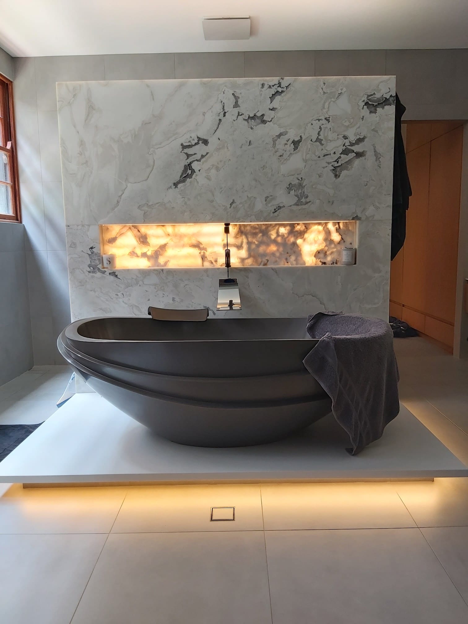 A bathtub in a bathroom with a marble wall behind it.