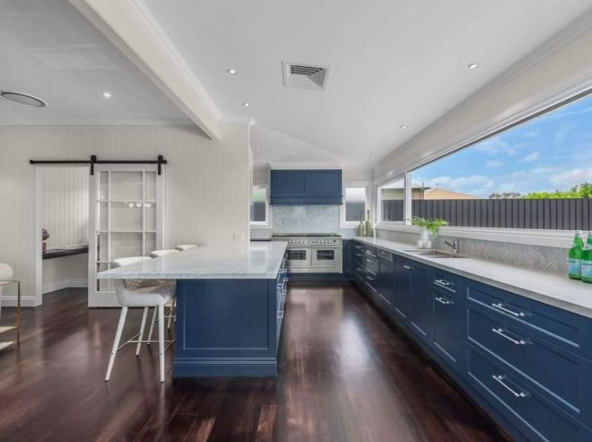 A kitchen with blue cabinets and white counter tops and a large window.