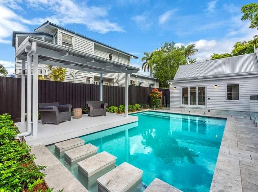 There is a large swimming pool in the backyard of a house.