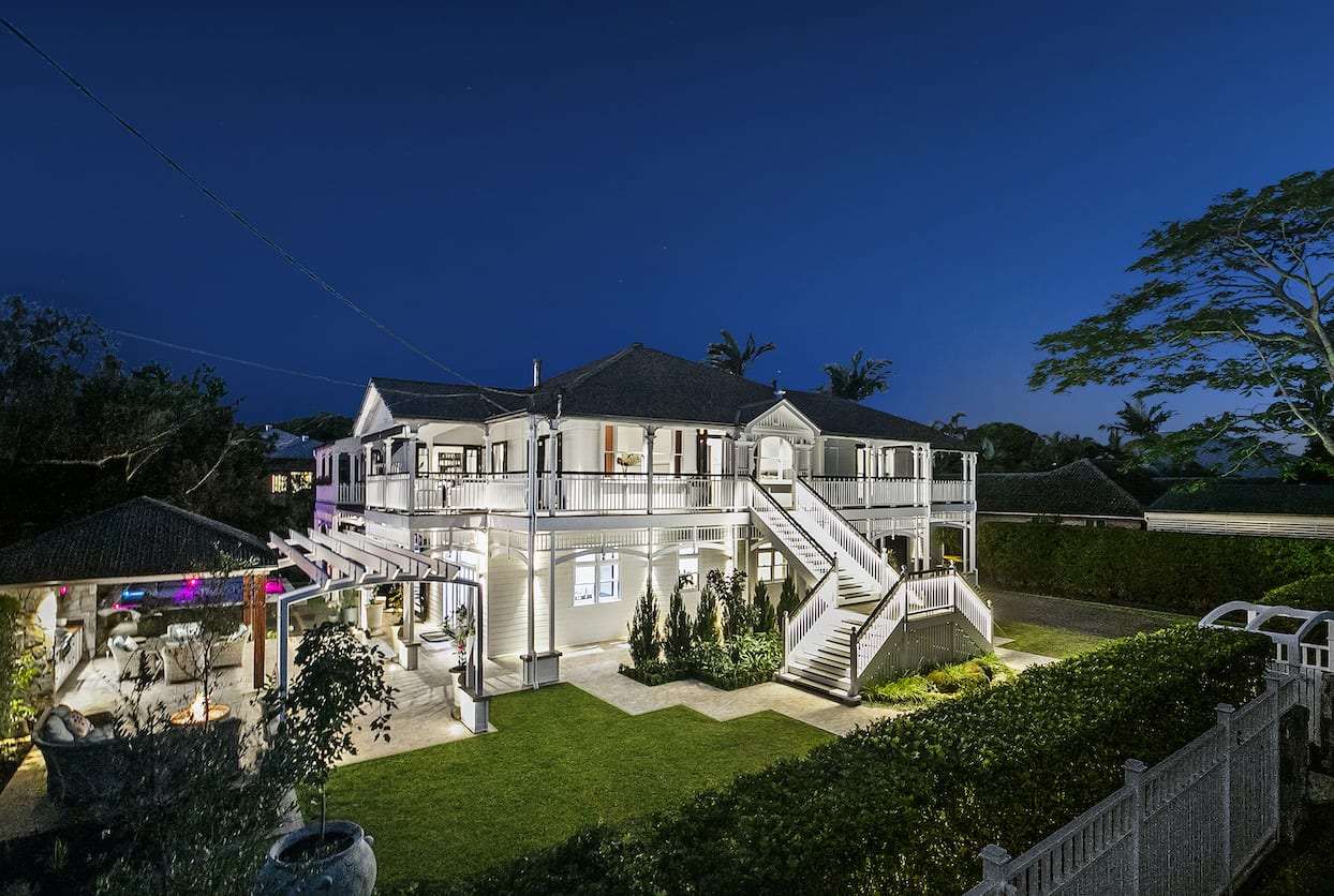 A large white house with stairs leading up to it is lit up at night.