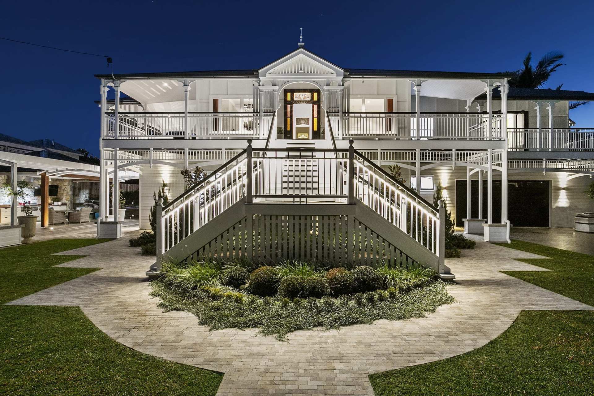 A large white house with stairs leading up to it is lit up at night.