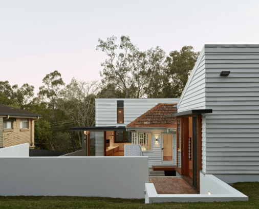 A white house with a red tile roof is surrounded by trees